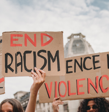 People are marching on strike against racism in the city. They are holding cardboard signs.